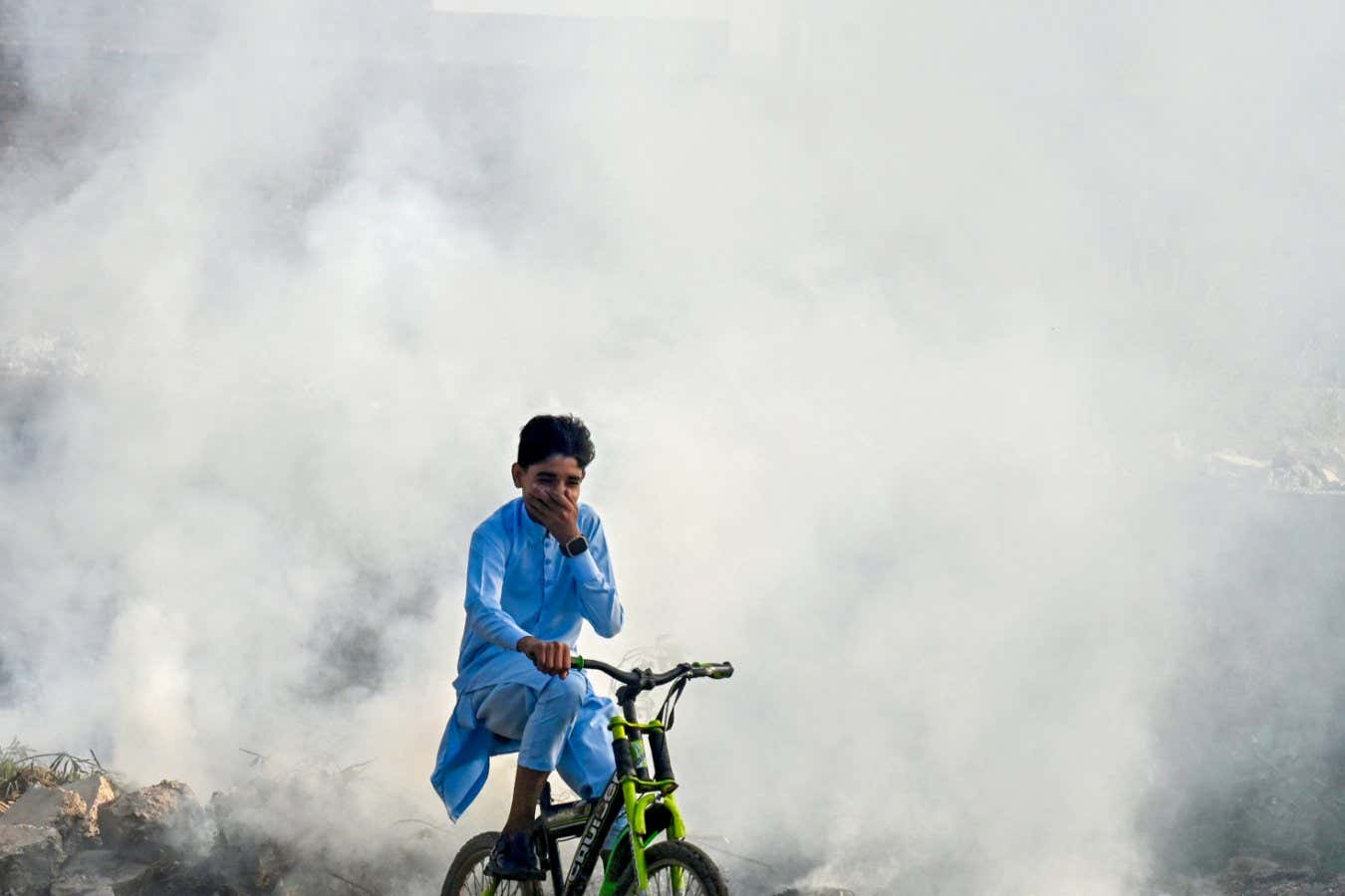 TOPSHOT - A boy rides past as smoke billows from a burning garbage dump, in Lahore on November 1, 2024. (Photo by Arif ALI / AFP) (Photo by ARIF ALI/AFP via Getty Images)