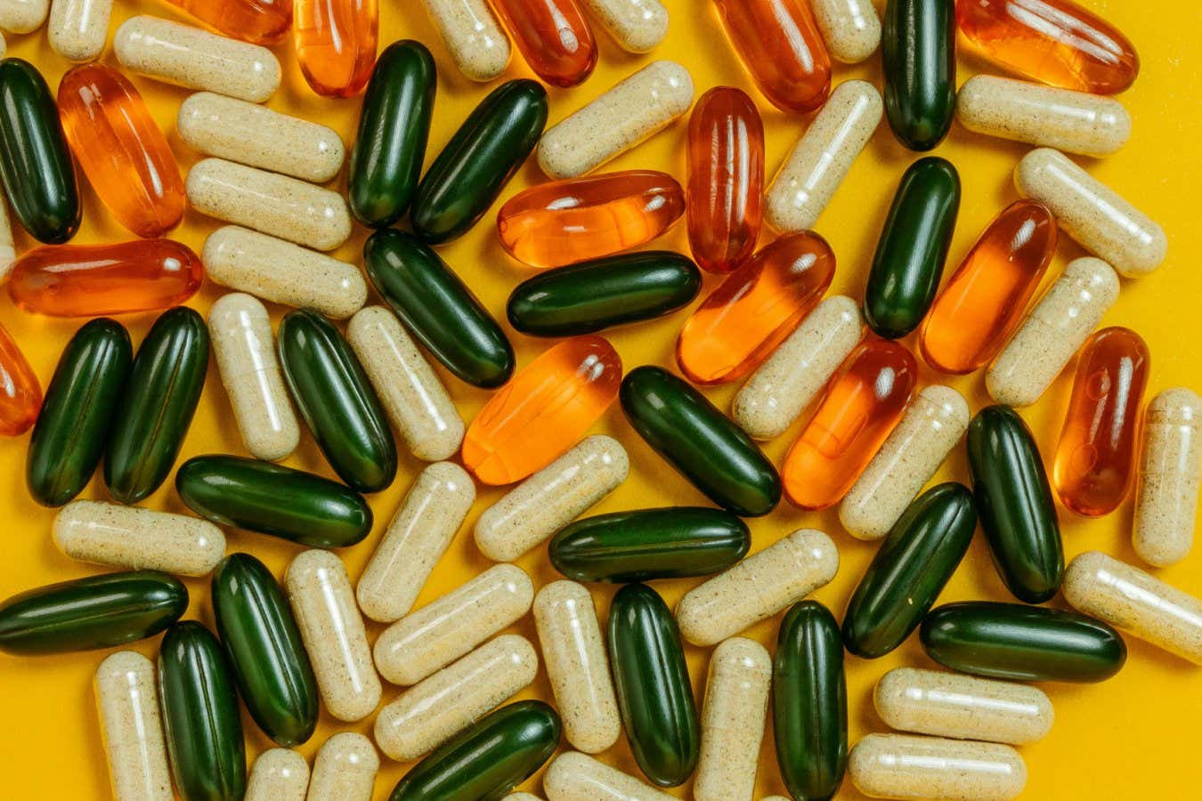 A pile of colourful supplement pills lying on a yellow table top.