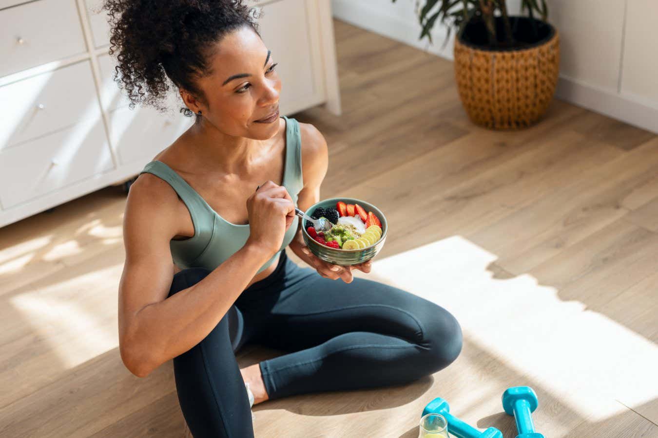 A woman eating a bowl of fruit while wearing exercise clothes