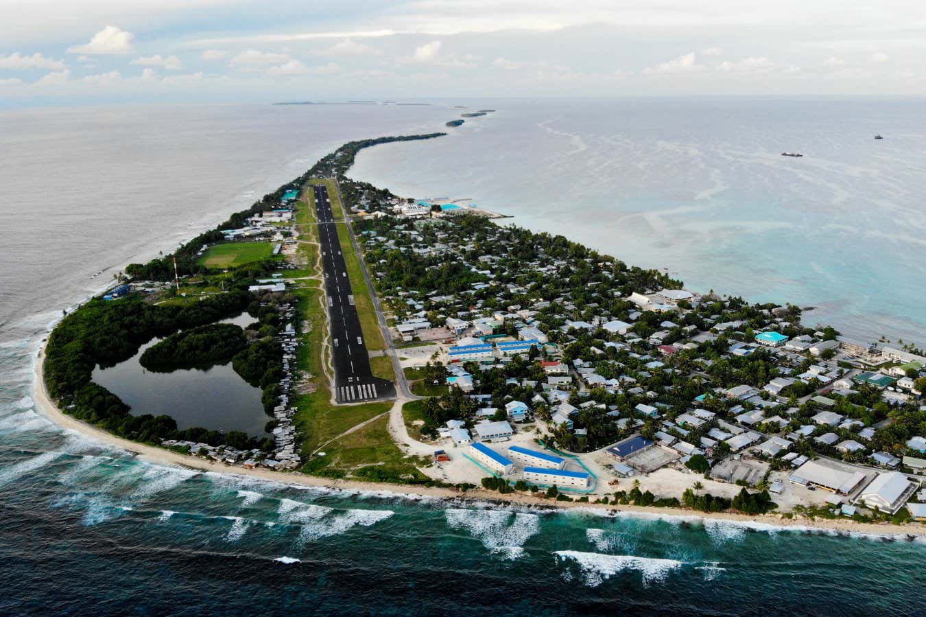 FUNAFUTI, TUVALU - NOVEMBER 28: An aerial view of downtown and the airport runway, between the Pacific Ocean (L) and lagoon (R), on November 28, 2019 in Funafuti, Tuvalu. The??low-lying??South Pacific island nation??of about 11,000 people has been classified as ???extremely vulnerable??? to climate change by the??United Nations Development Programme.??The world???s fourth-smallest country is struggling to cope with climate change related impacts including five millimeter per year sea level rise (above the global average), tidal and wave driven flooding, storm surges, rising temperatures, saltwater intrusion and coastal erosion on its nine coral atolls and islands, the highest of which rises about 15 feet above sea level. In addition, the severity of cyclones and droughts in the Pacific Island region are forecast to increase due to global warming. Some scientists have predicted that Tuvalu could become inundated and uninhabitable in 50 to 100 years or less if sea level rise continues.??The country is working toward a goal of 100 percent renewable power generation by 2025 in an effort to curb pollution and set an example for larger nations. Tuvalu is also exploring a plan to build an artificial island. (Photo by Mario Tama/Getty Images)