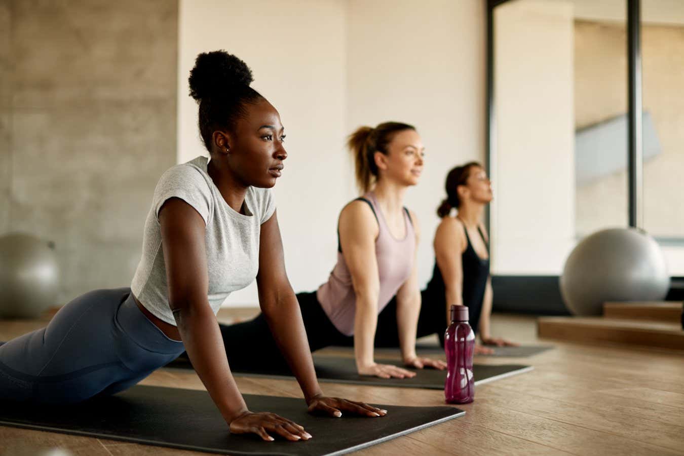 Athletic women doing stretching wile exercising on group training in a gym. Focus is on African American woman.; Shutterstock ID 2039901623; purchase_order: -; job: -; client: -; other: -