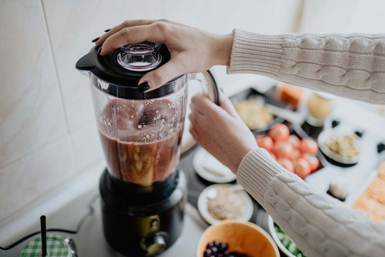 Woman holding blender and making healthy smoothie with various vegetables and fruits in the kitchen at home