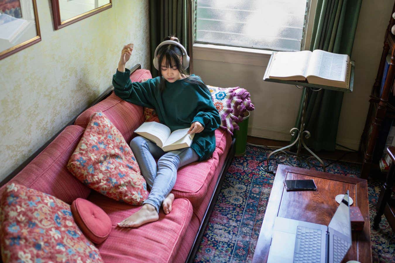 A young woman reading a book while wearing headphones.