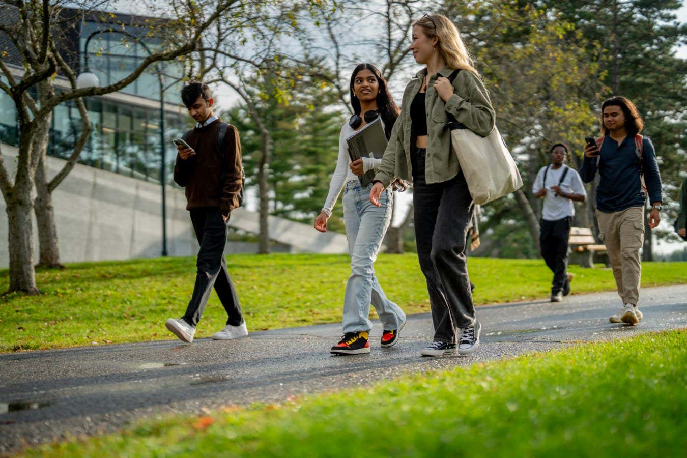A group of university students are seen walking outside on campus as they make their way from residence to class. They are each dressed casually and have backpacks and book bags with them.